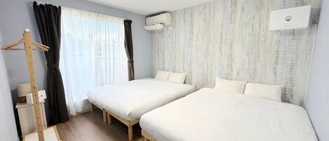 A room with two single beds, a wooden hanger, a standing heater, and an air conditioning unit.