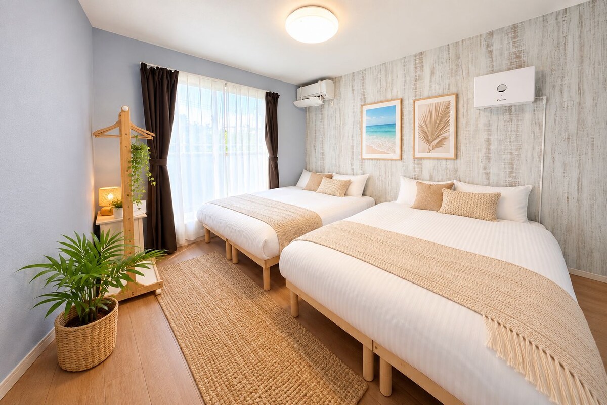 A hotel room with two beds, a large window with curtains, a wall-mounted air conditioner, and framed pictures.