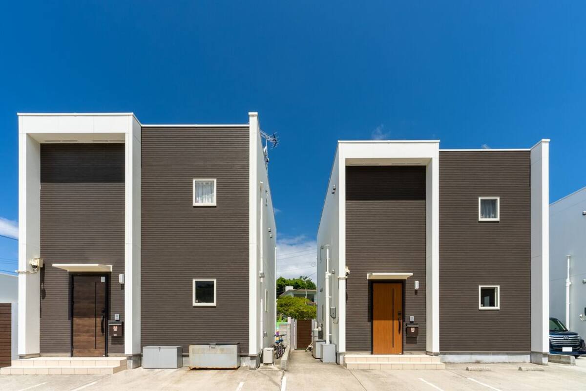 Une rangée d’immeubles modernes à deux étages, dotés d’une façade uniforme, d’une allée centrale et surplombés par un ciel d’un bleu éclatant.