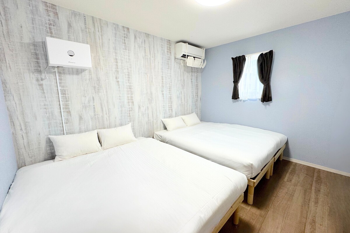Una habitación con dos camas, aire acondicionado en la pared y una ventana con cortinas.