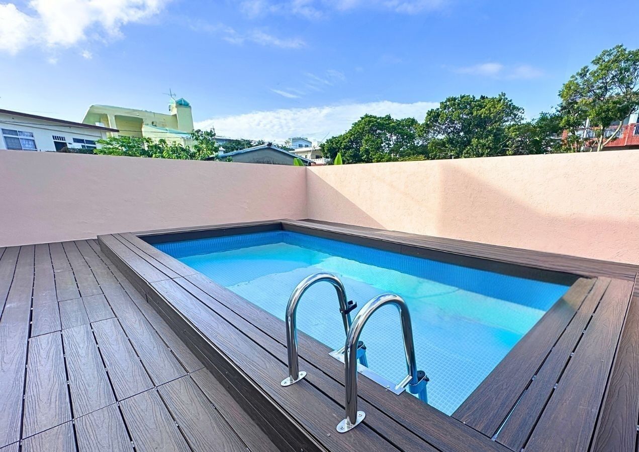 Una piscina rettangolare con bordo in legno e scalette metalliche, circondata da un muretto basso e alberi sullo sfondo.