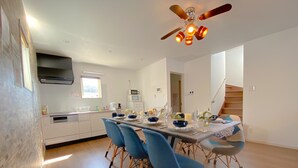 A modern kitchen with white cabinets, a built-in oven, and a microwave. There is a dining table with blue chairs and a ceiling fan above. - Grandioso Okinawa Pool Villa Onna 4 (Onna)