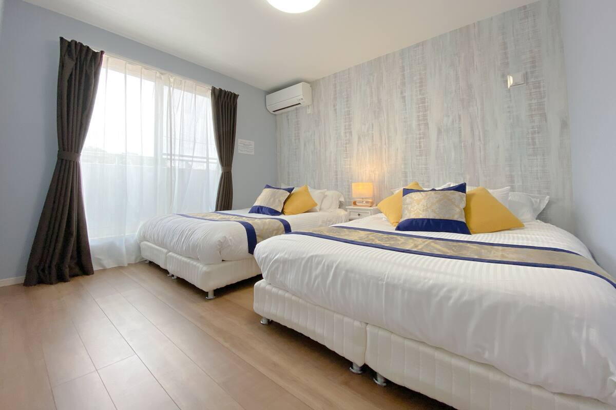 Une chambre d’hôtel avec deux lits, une table de chevet avec une lampe et une grande fenêtre avec des rideaux.