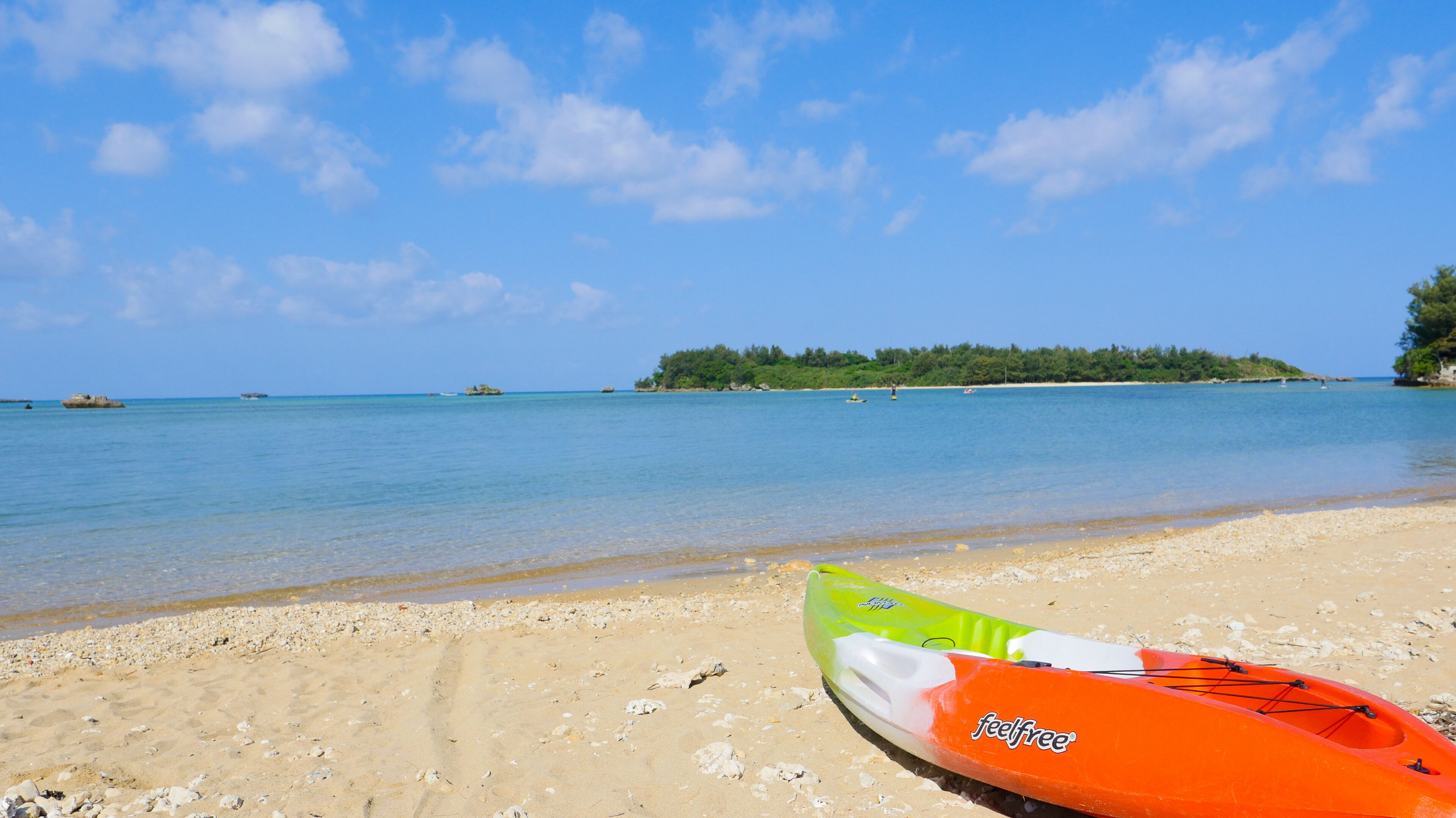 A kayak on a sandy beach with clear blue water and a distant island.