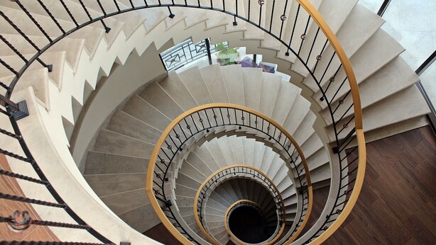 A spiral staircase with a wooden handrail and black metal balusters.