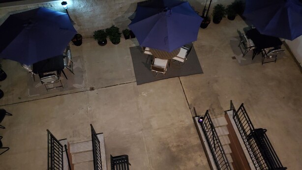 Een terras buiten met meerdere blauwe parasols, een zithoek met stoelen en een tafel, en potplanten.