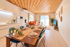 A modern kitchen with white cabinets, a wooden ceiling, and a dining area with a long table set for six.