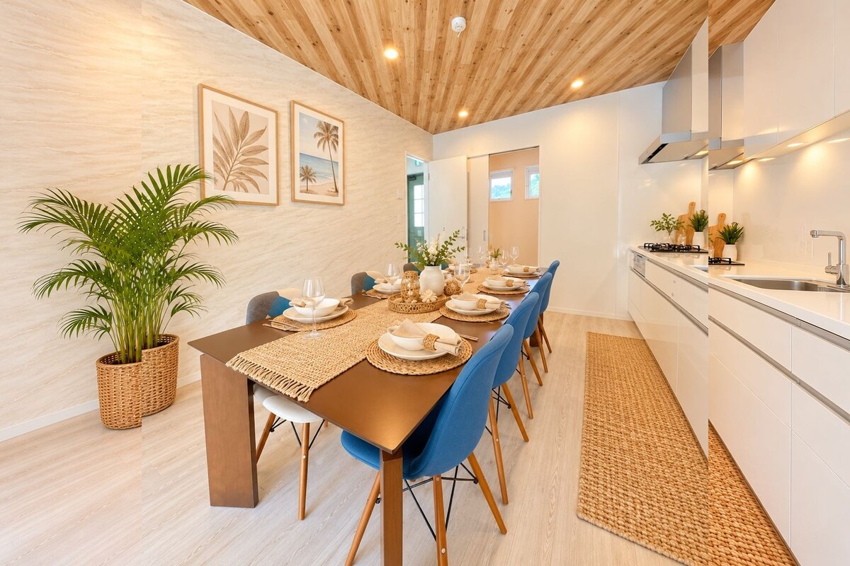 A modern dining area with a long table set for six, wooden flooring, and a kitchen with white cabinets and a stainless steel sink.