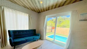 A room with a blue sofa, a small table, a brick wall, and a large sliding glass door leading to a pool. - Grandioso Okinawa Pool Villa Onna 6 (Onna)