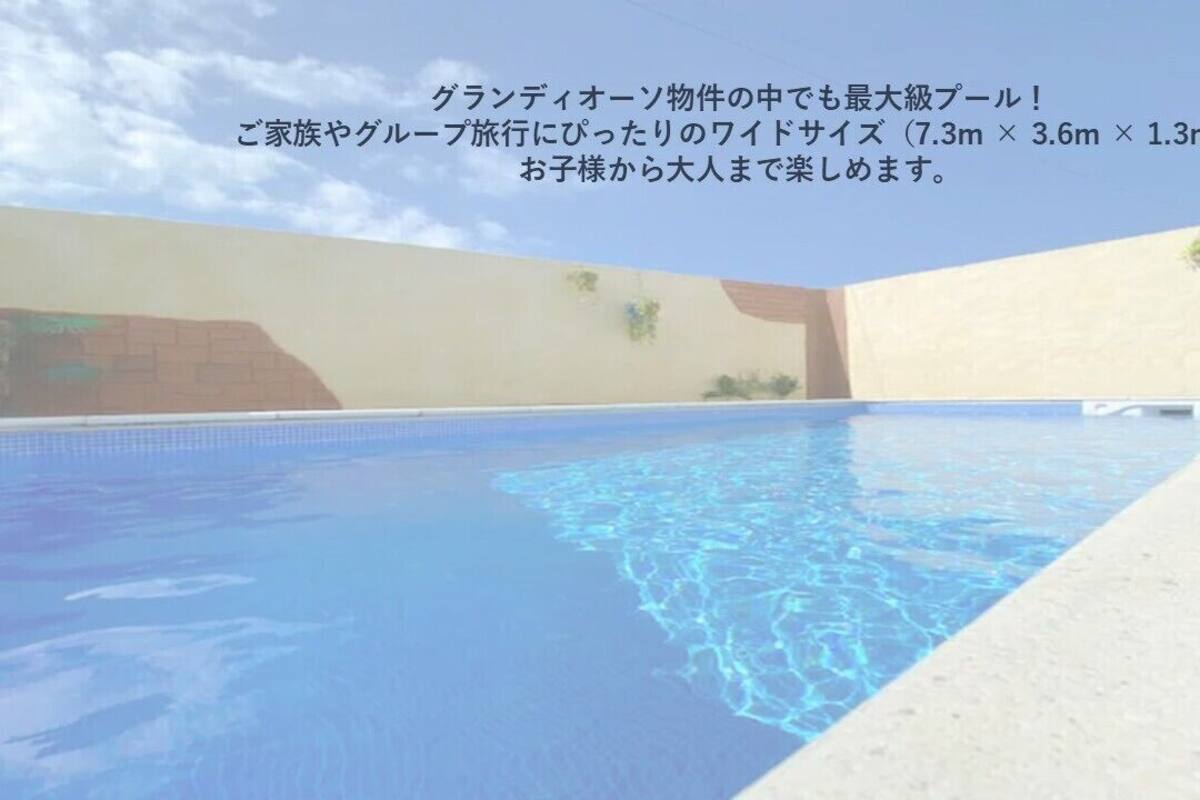 A swimming pool with clear blue water, surrounded by a concrete deck and a beige wall.