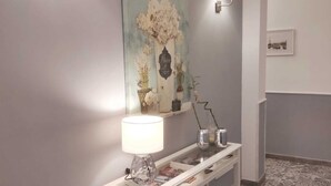 Un pasillo con una consola blanca, una lámpara de pared y una obra de arte enmarcada encima.