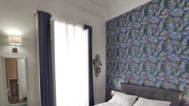 Una habitación de hotel con una cama, una silla, una mesa con un libro y un papel tapiz estampado.