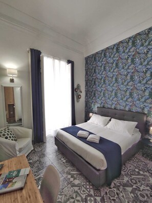 Una habitación de hotel con una cama, una silla, una mesa con un libro y un papel tapiz estampado.