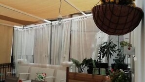 Un espacio al aire libre cubierto con una mesa y sillas, una maceta colgante con flores amarillas y plantas en macetas.