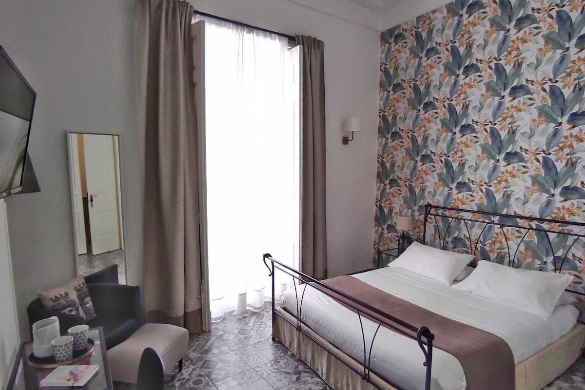 Une chambre d’hôtel avec un lit, un bureau et une chaise, un miroir et un mur décoré d’un motif.