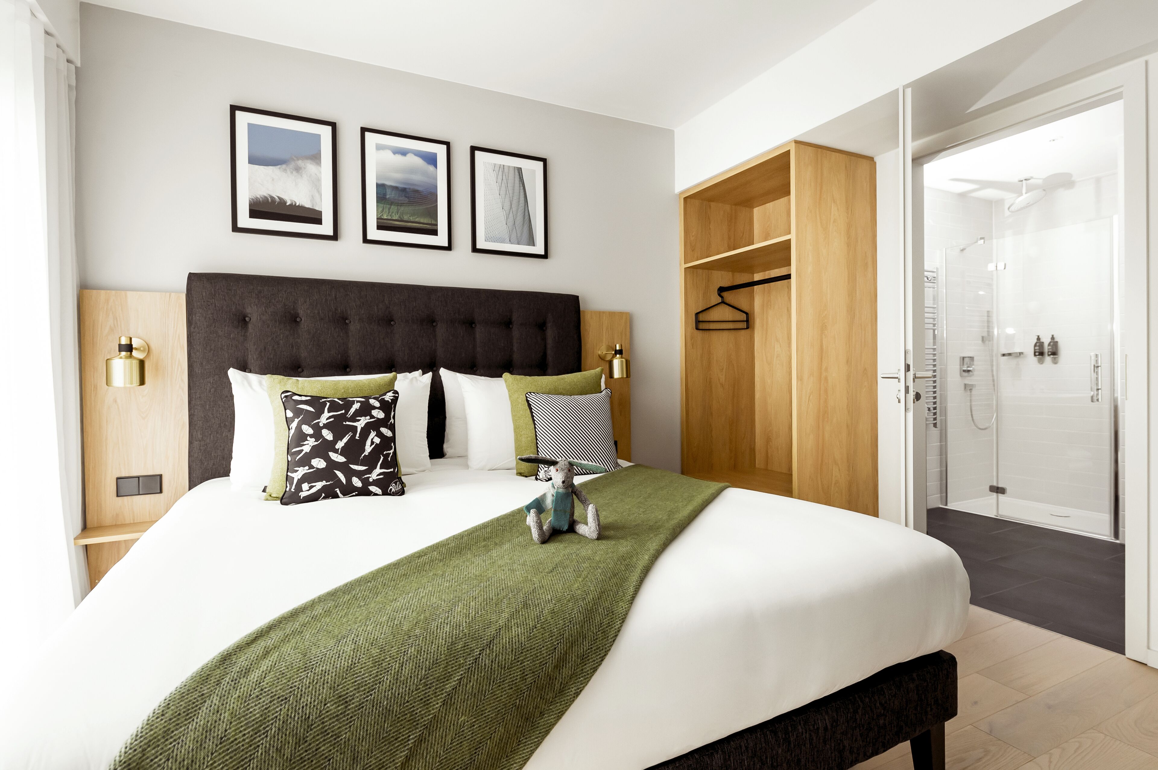 A hotel room with a large bed, a wooden wardrobe, a shower area, and framed pictures on the wall.