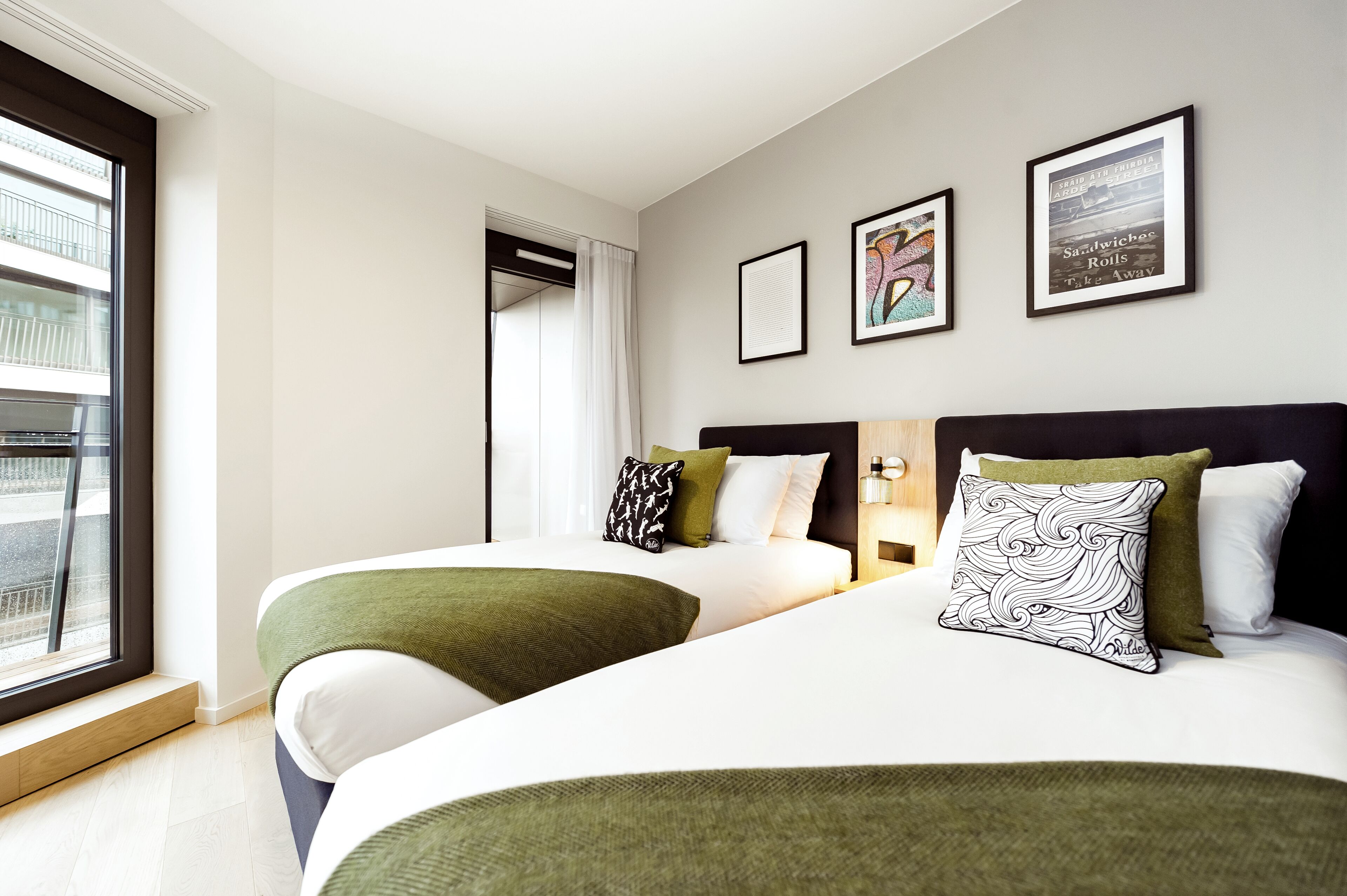 Een hotelkamer met twee bedden, een raam met uitzicht en kunstwerken in lijsten aan de muur.