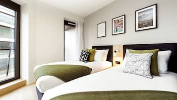 Een hotelkamer met twee bedden, een raam met uitzicht en kunstwerken in lijsten aan de muur.