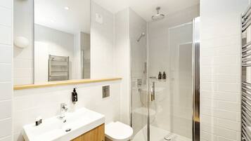 Un baño moderno con lavamanos blanco, espejo y cabina de ducha de vidrio.