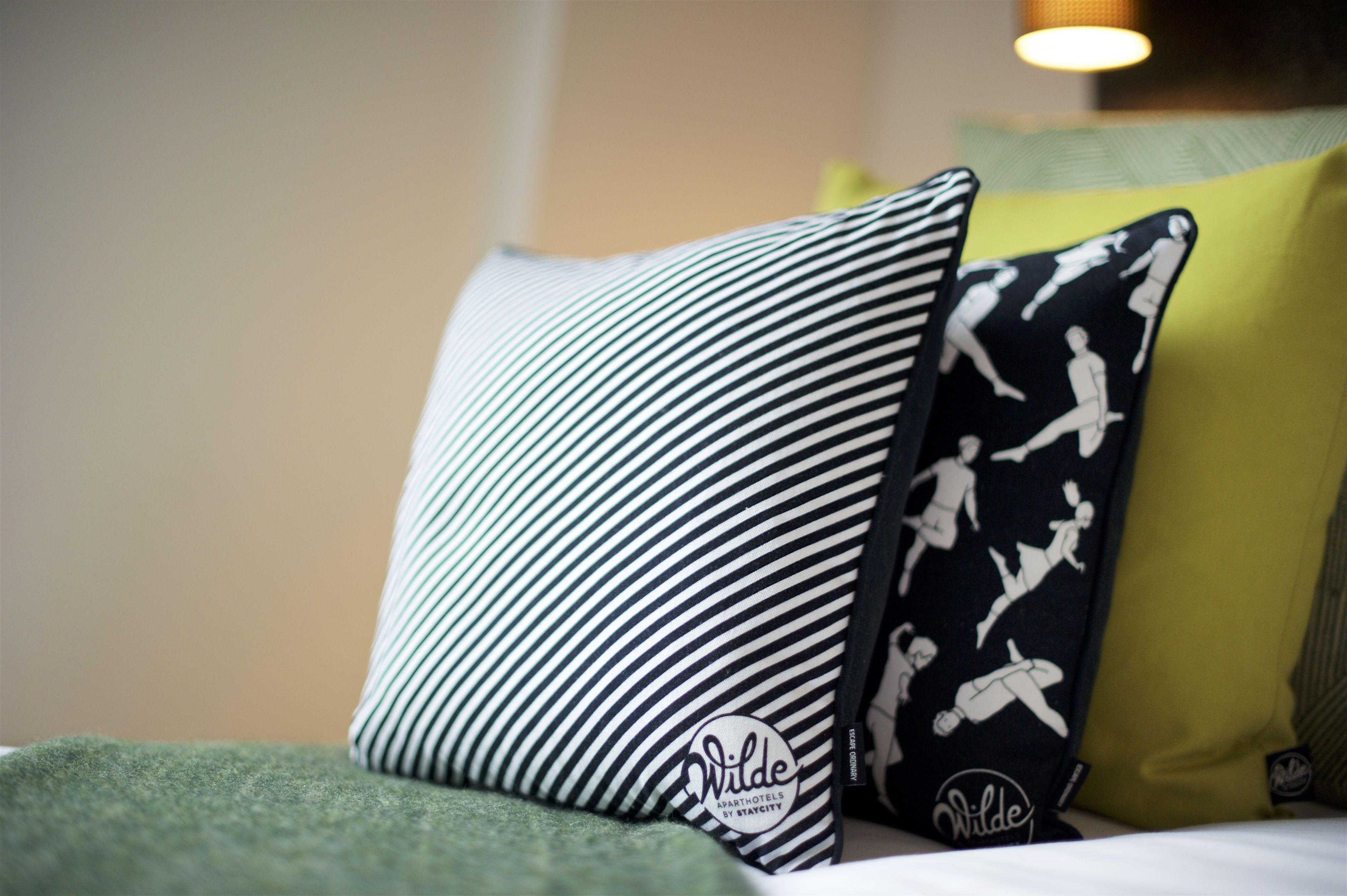 A bed with a green blanket and two pillows, one striped and one with a sports pattern.