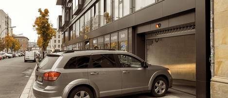 A modern building with a garage entrance, parked cars, and autumn trees.