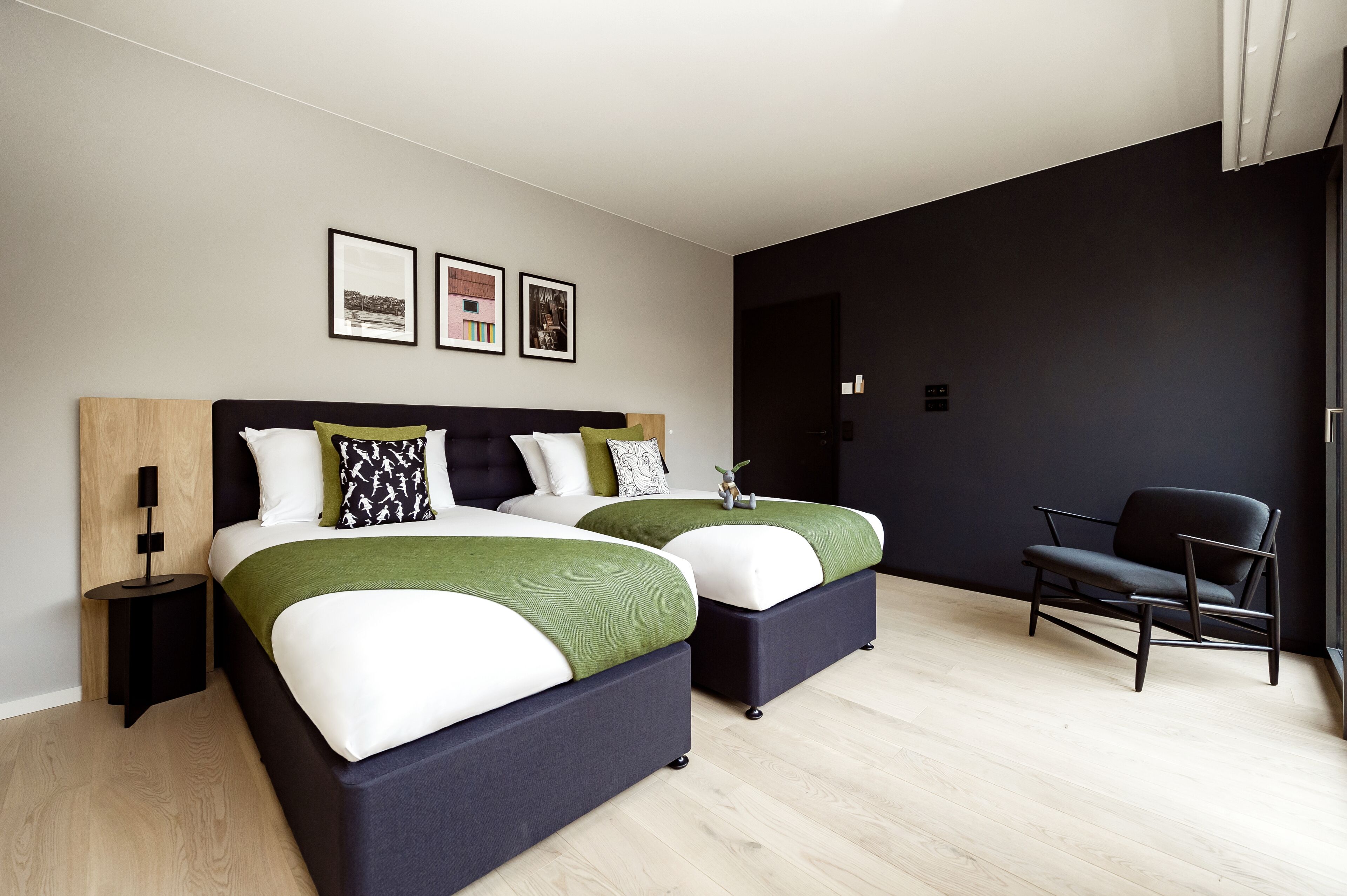 A modern hotel room with two beds, a dark accent wall, and a minimalist design.