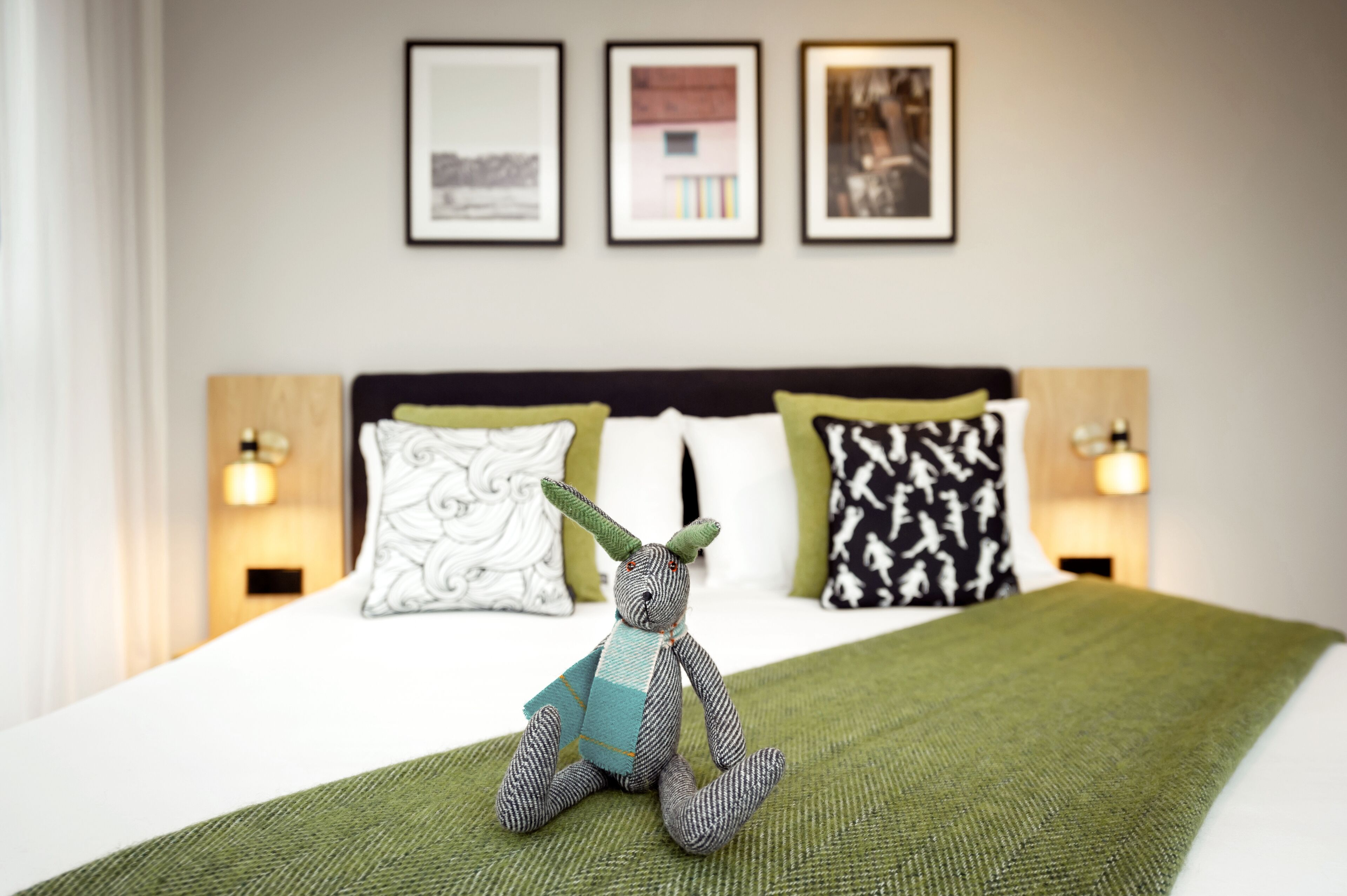 A bed with a green blanket, a decorative pillow, and a small stuffed toy on the bed.
