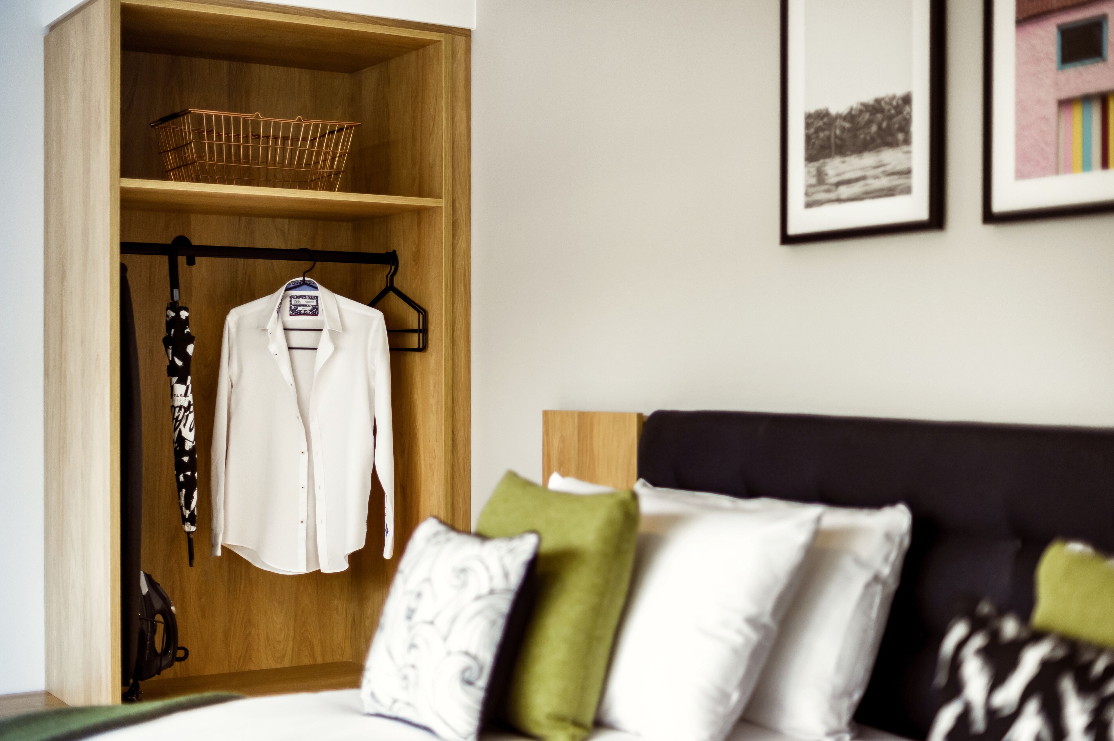 A neatly organized bedroom with a wooden wardrobe, a bed with pillows, and a framed picture on the wall.