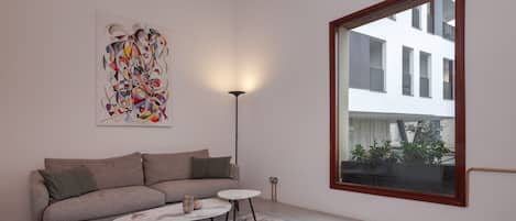 A modern living room with a sofa, a coffee table, a floor lamp, and a large window.