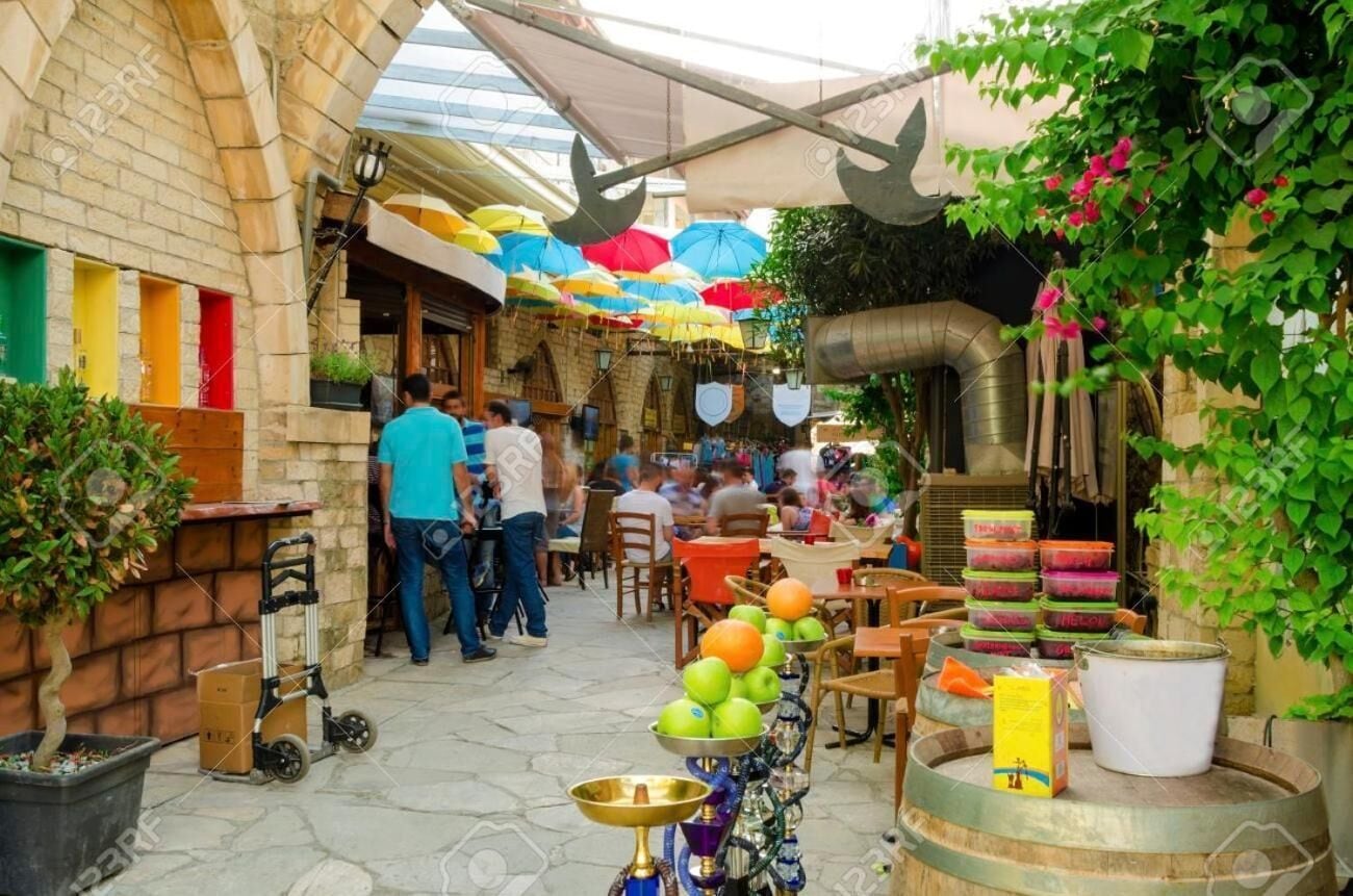 Un mercado al aire libre con varios puestos, una galería techada y gente comprando.
