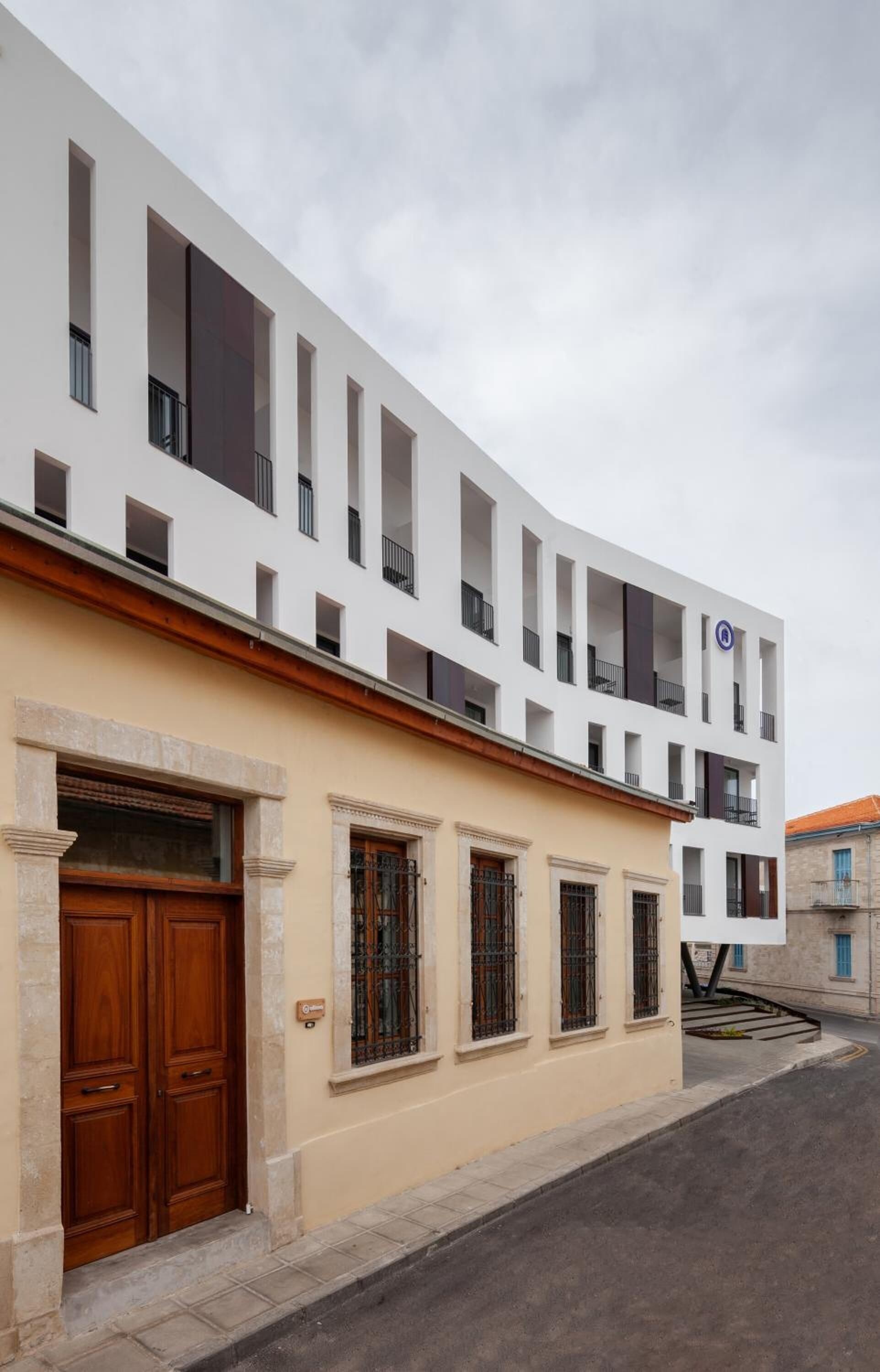 A modern building with a white facade, large wooden doors, and multiple windows.