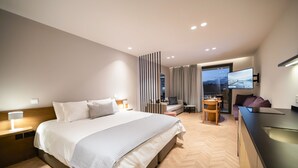 Habitación de hotel moderna con una cama grande, un escritorio, un sofá, un televisor y vistas a la ciudad.