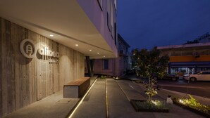 Una entrada de hotel moderna con fachada de madera, un banco y un camino bien iluminado que lleva a la entrada.