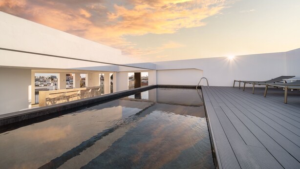 Una piscina en la azotea con vistas despejadas del paisaje urbano, un cielo iluminado por el sol y una terraza de madera.