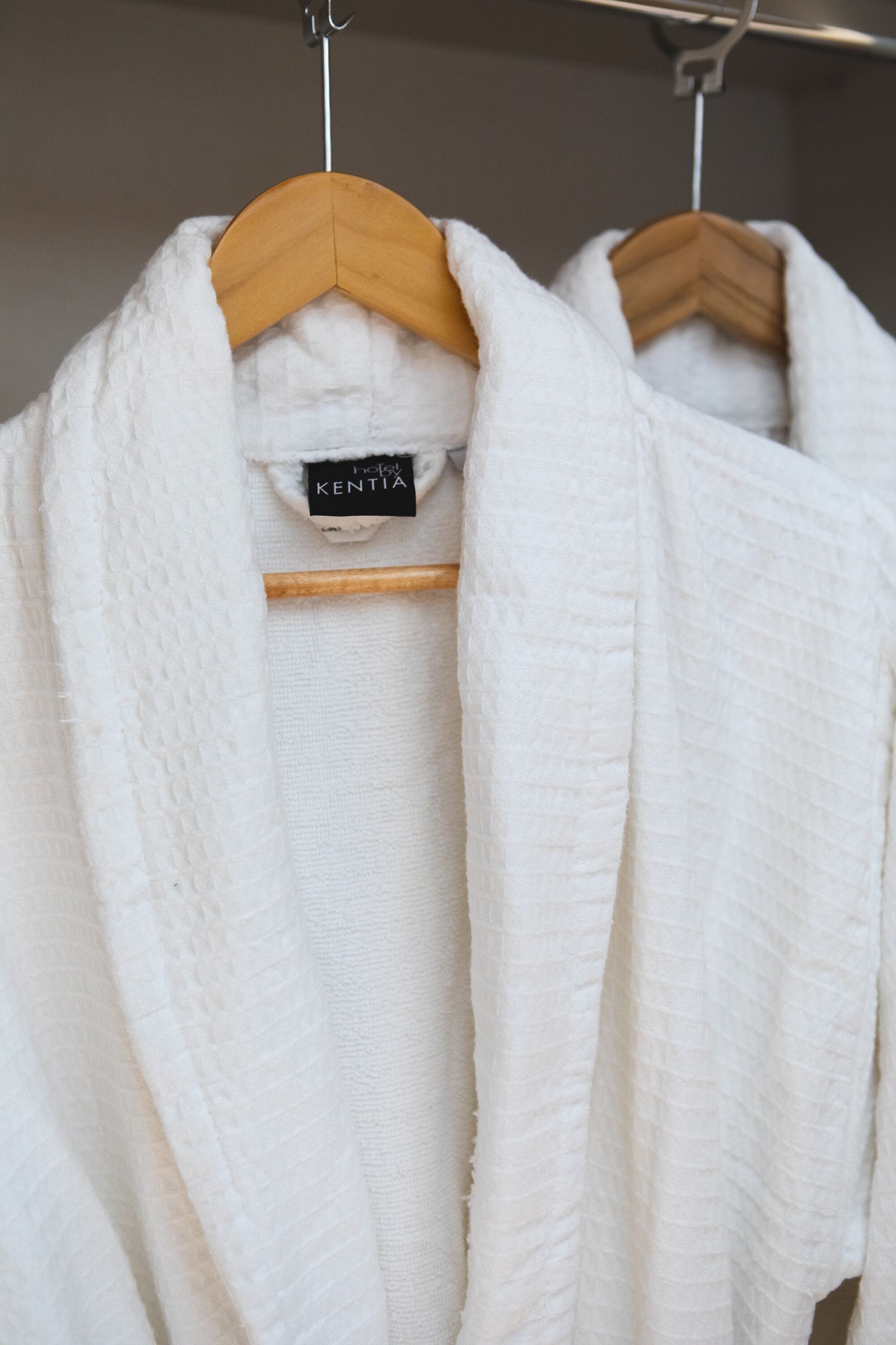 A white robe hanging on a wooden hanger with a tag labeled "Hotel Kentia".