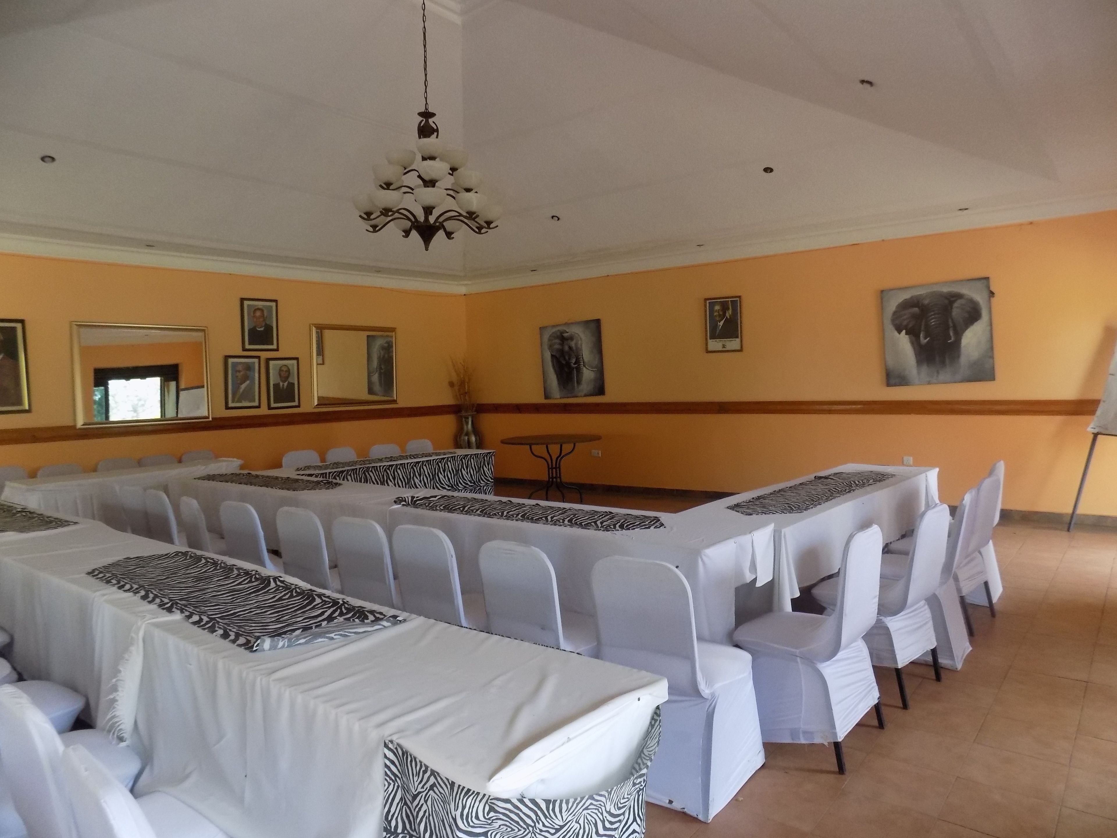 Un salón de conferencias con mesas y sillas blancas, una araña de cristal, retratos enmarcados y una pintura de un elefante en la pared.