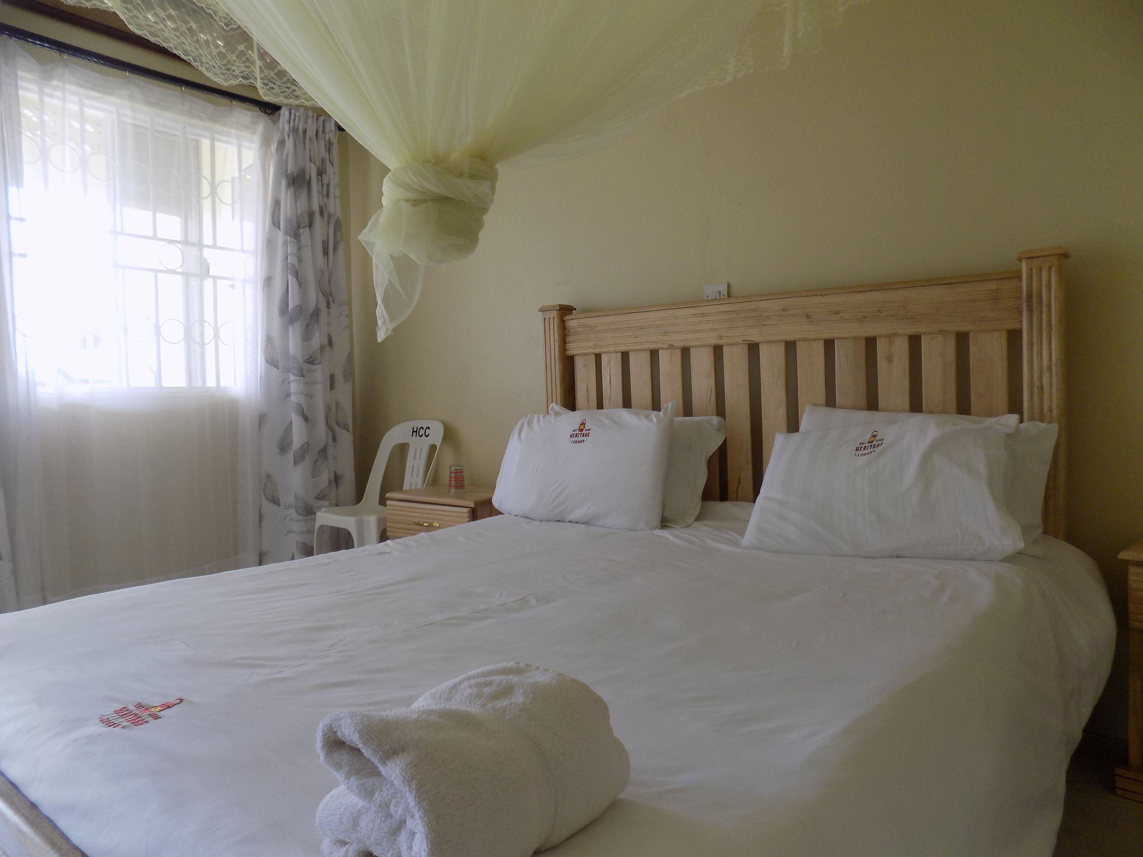 Een net opgemaakt bed met witte lakens en kussens, een houten hoofdbord en een nachtkastje met een kleine lamp.