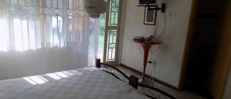 Une chambre à coucher comprenant un lit, une table de chevet, un téléviseur fixé au mur et une fenêtre avec des rideaux.