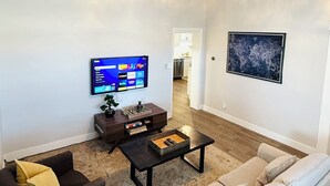 A living room with a flat-screen TV, a coffee table, a sofa, and a bookshelf. - The Cozy Murray Bungalow fast WIFI free parking!  (Murray)