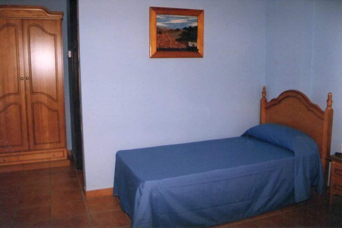 A bedroom with a single bed, a wooden wardrobe, and a framed picture on the wall.