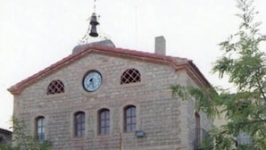 A stone building with a clock, a balcony, and a bench in front. - Los Trulls d'Auligué (La Pobla de Massaluca)