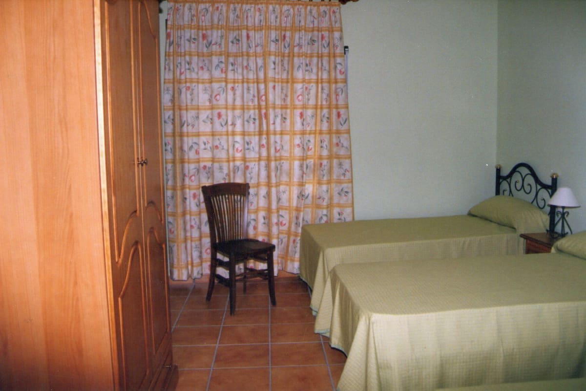 A room with two beds, a chair, a nightstand, and a curtain with a floral pattern.