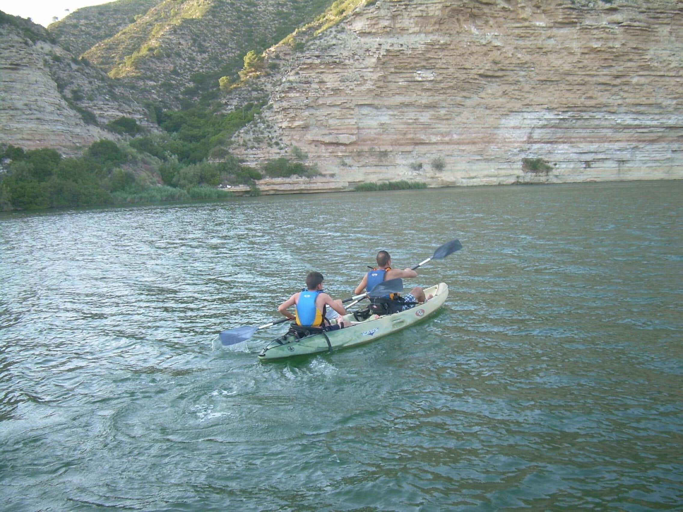 A kayak on a calm river with rocky cliffs in the background.