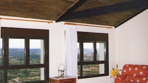 A spacious room with a high ceiling, large windows offering a view of the countryside, a wooden table with a vase, and a red sofa. - Los Trulls d'Auligué (La Pobla de Massaluca)