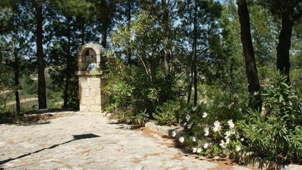 A stone pathway leading to a stone archway surrounded by greenery and trees. - Los Trulls d'Auligué (La Pobla de Massaluca)