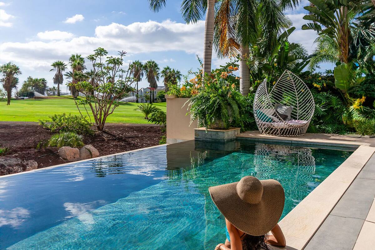 A swimming pool with clear blue water, surrounded by tropical plants and palm trees.