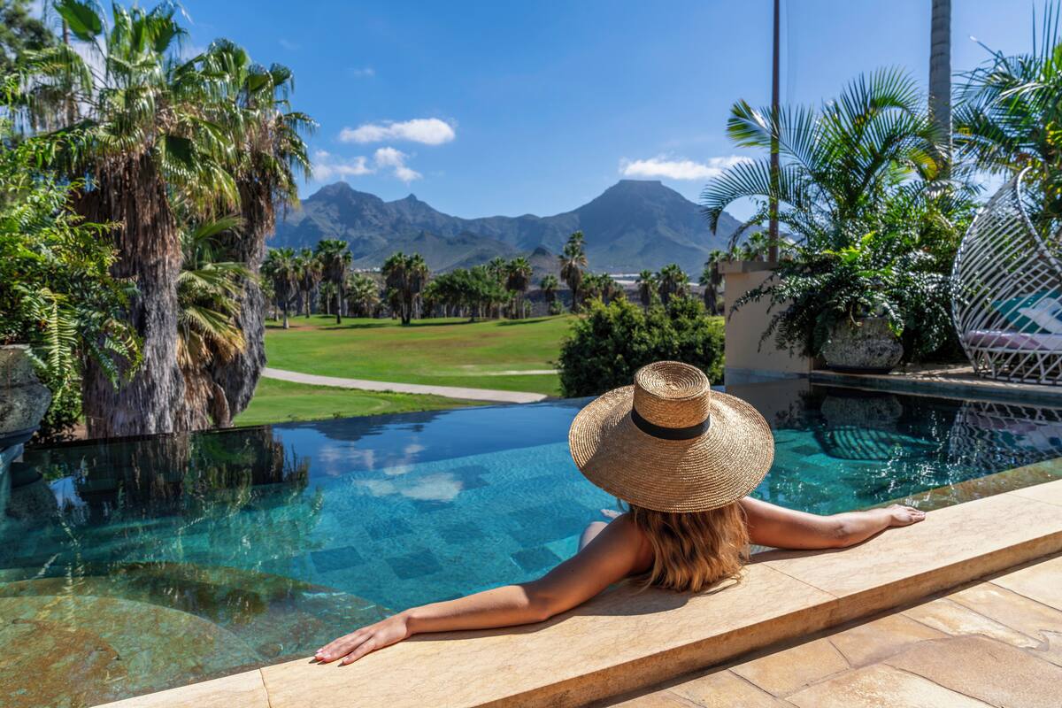 A person relaxing by a pool with a view of a golf course and mountains.