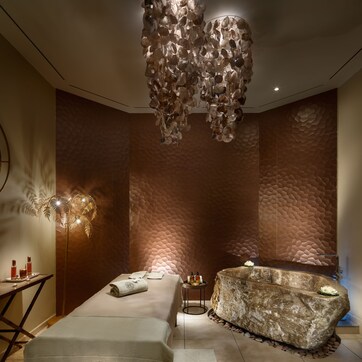 A spa room with a massage table, a stone bath, and a wall with a textured pattern.