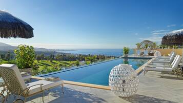 A poolside area with lounge chairs, a pool, and a view of the ocean and cityscape.