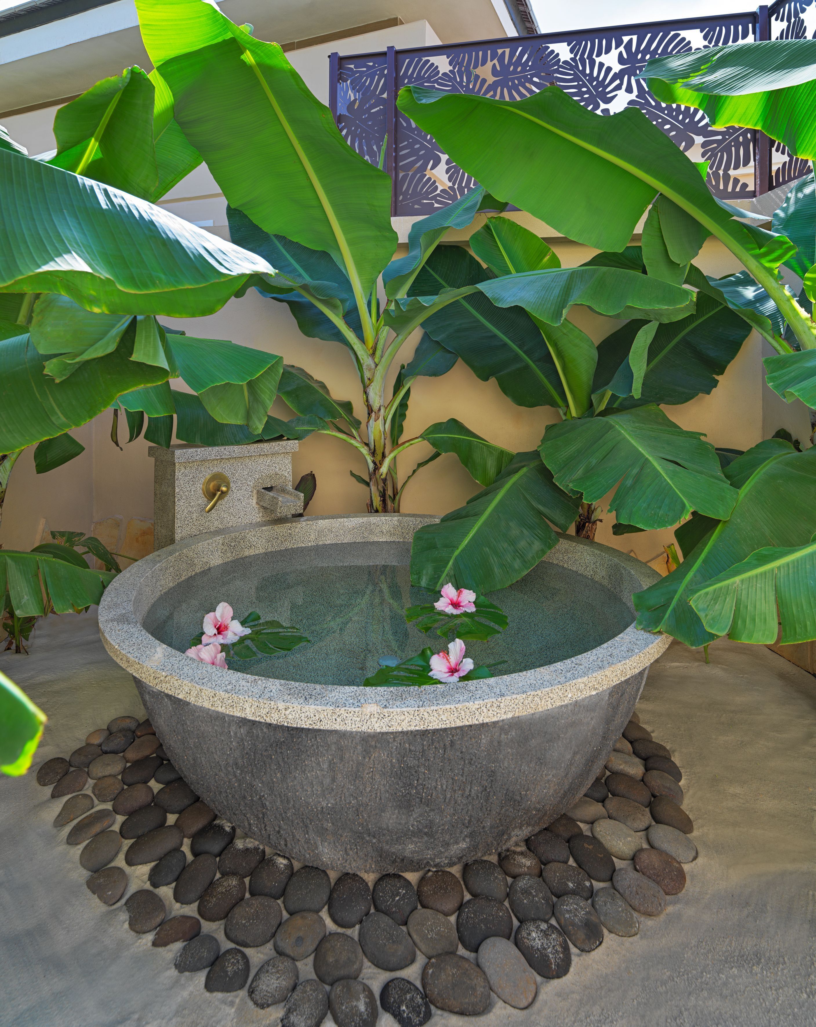 A stone hot tub surrounded by rocks and large green leaves.